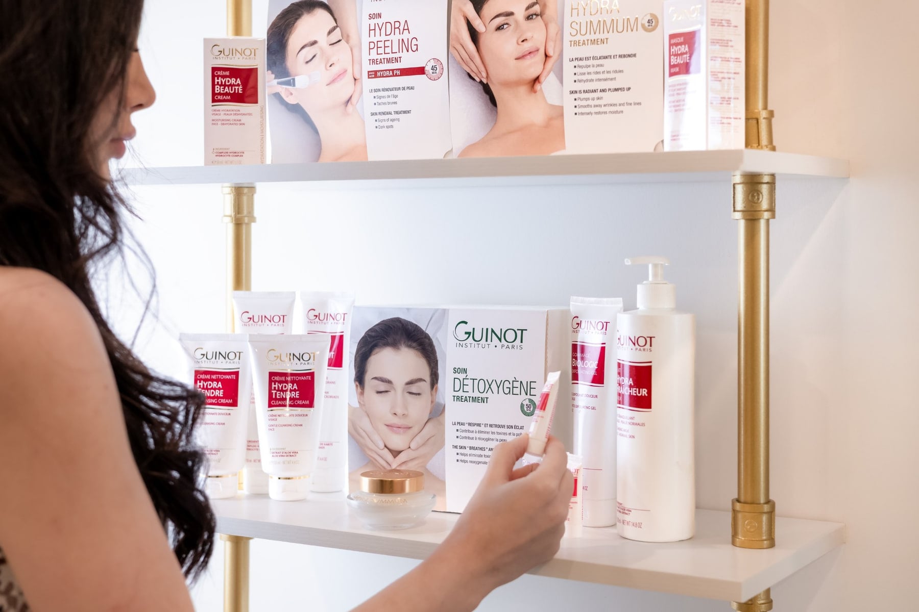 Shiva choisissant un produit Guinot sur les tablettes de CHIC, parmi les soins Hydra Peeling, Hydra Summum et Détoxygène